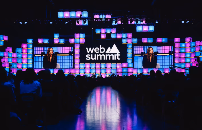 A large stage viewed over the silhouetted heads of a packed audience. A line of people stands on the stage, facing towards the audience. Confetti fills the air. A large Web Summit Rio logo hangs in the center of the stage. Two screens on either side of the logo read 'That's all for today!'